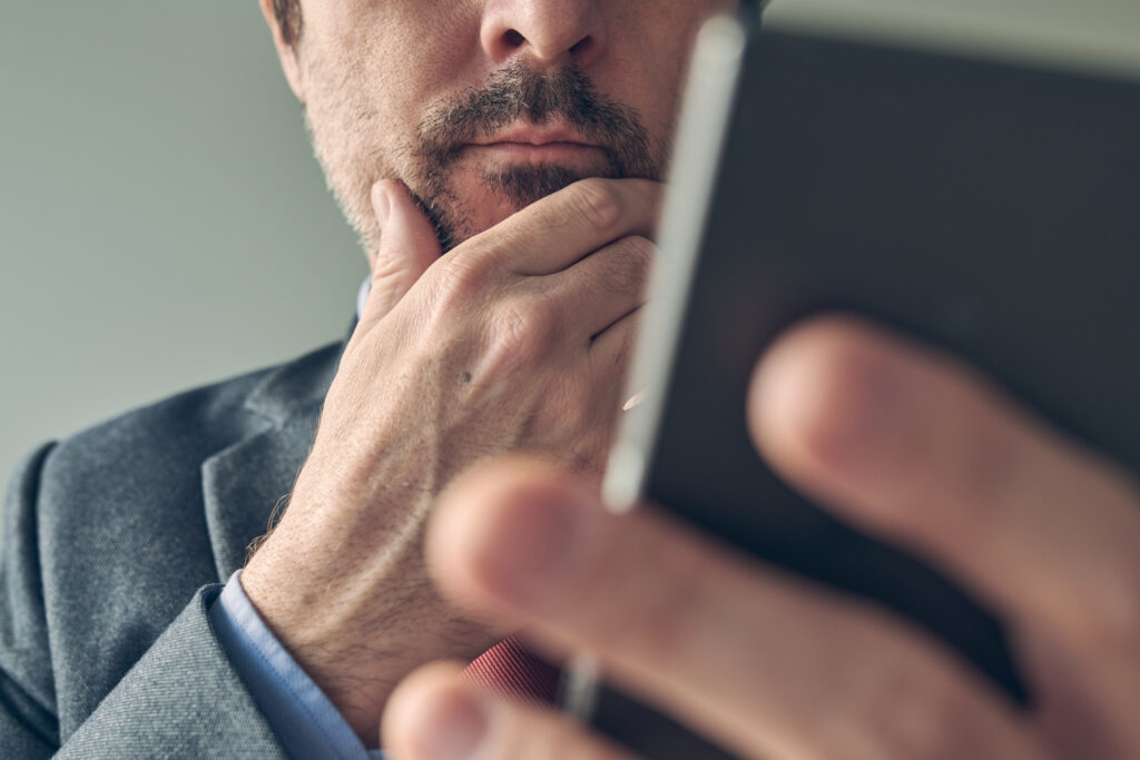 Worried businessman looking at mobile phone screen, close up with selective focus